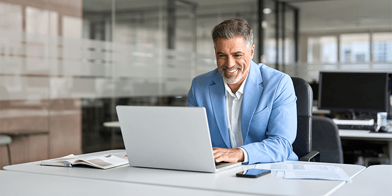 Man in blue shit sitting at table working on a laptop